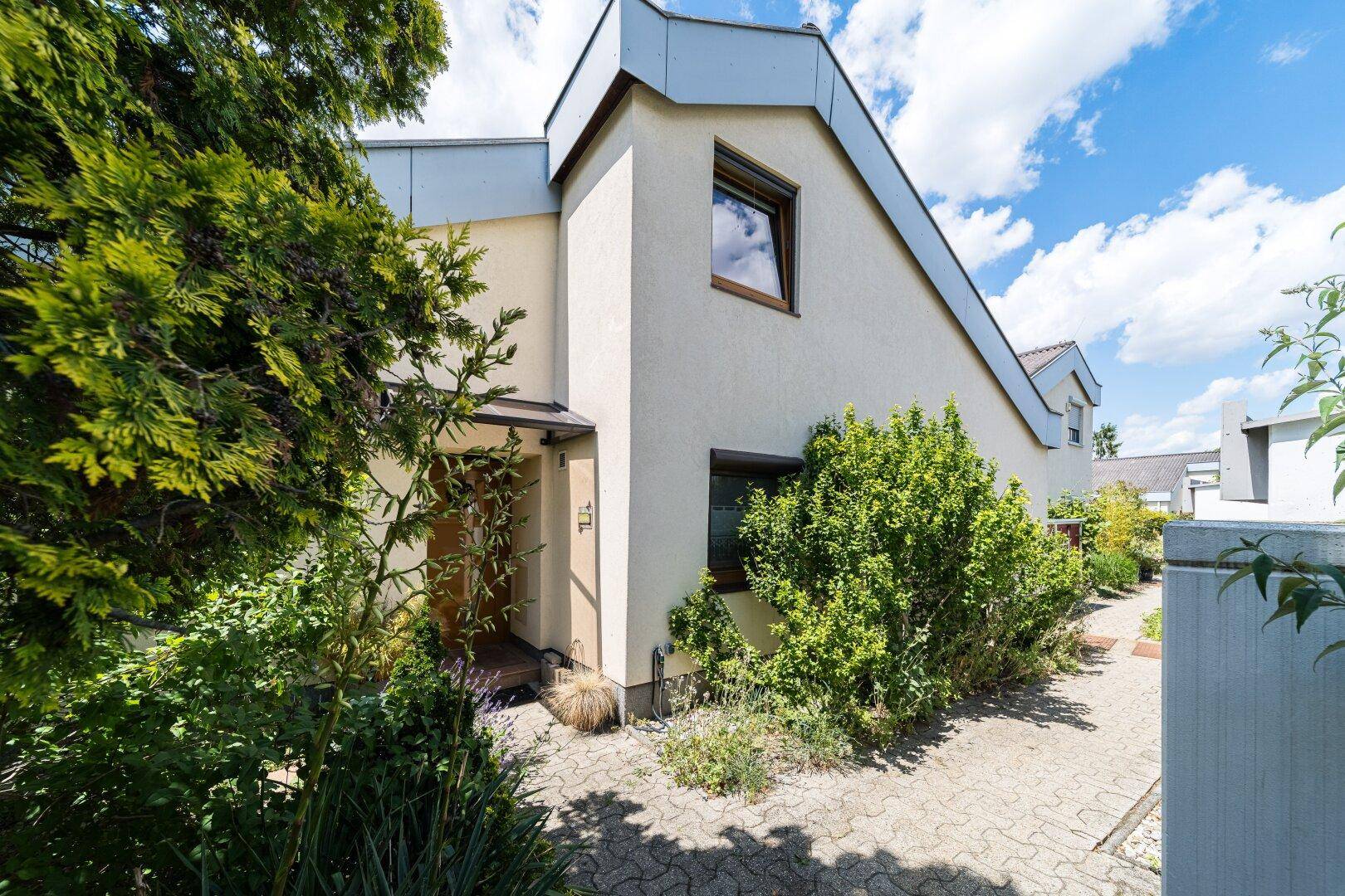Modernes Reihenhaus mit gepflegtem Vorgarten und Eingangsbereich unter blauem Himmel.