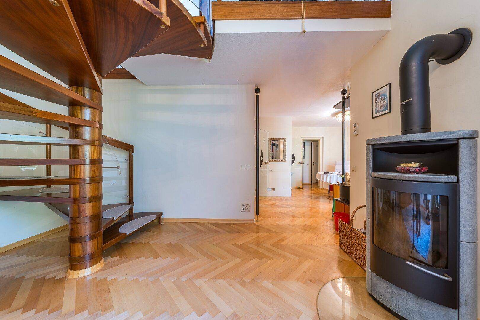 Detailansicht des Kaminofens und der eleganten Holzwendeltreppe im offenen Wohnbereich.