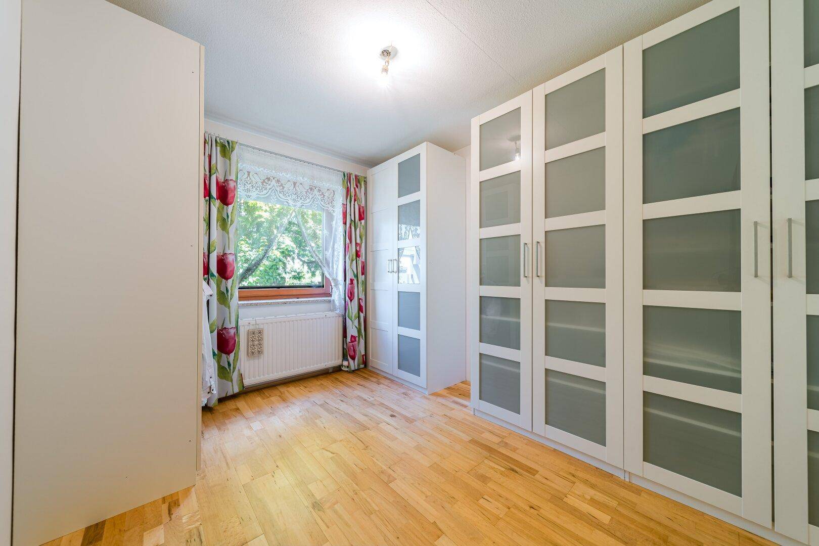 Schlafzimmer mit hellem Parkettboden und großen weißen Kleiderschränken.