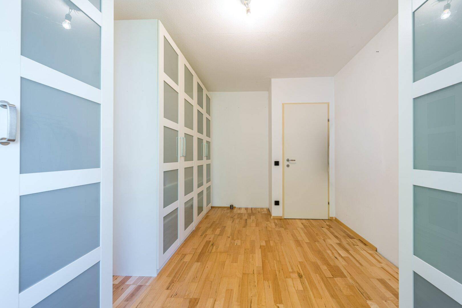 Geräumiges Zimmer mit Holzboden und modernen weißen Schränken.