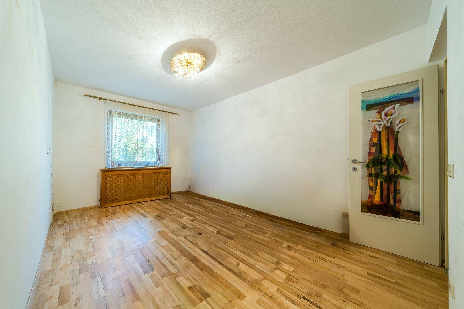Helles Zimmer mit Holzboden und einem Fenster, bereit zur individuellen Gestaltung.