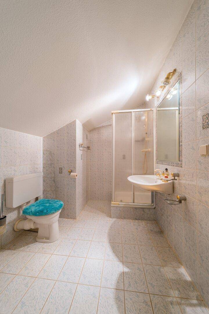 Badezimmer im Dachgeschoss mit Dusche, Waschtisch und hellen Fliesen.