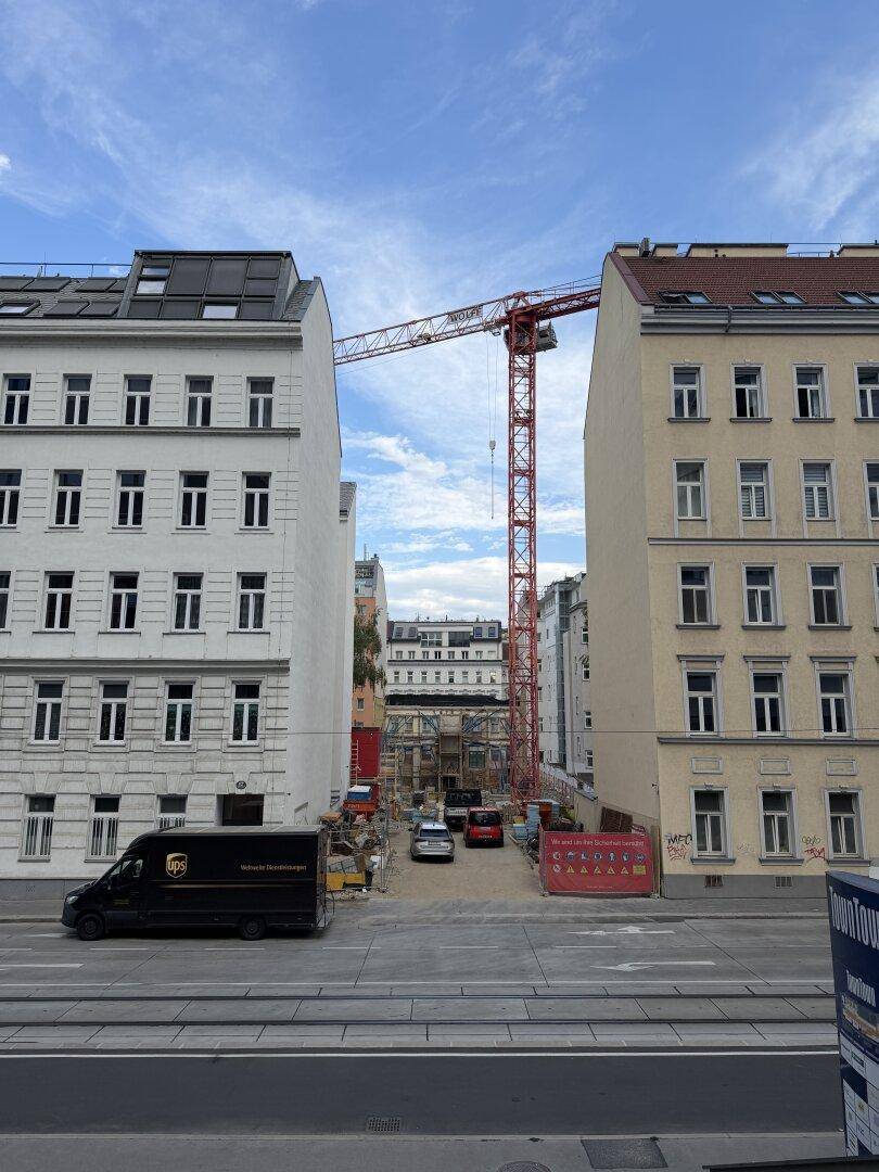 Blick auf eine städtische Baustelle mit einem großen roten Kran zwischen zwei Altbauten.