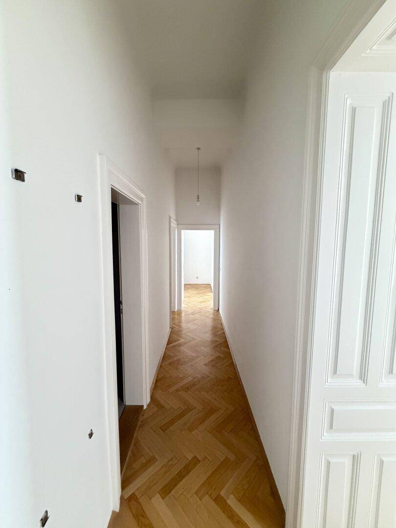 Langer, heller Flur mit Fischgrätparkett, der zu weiteren Räumen in der Wohnung führt.