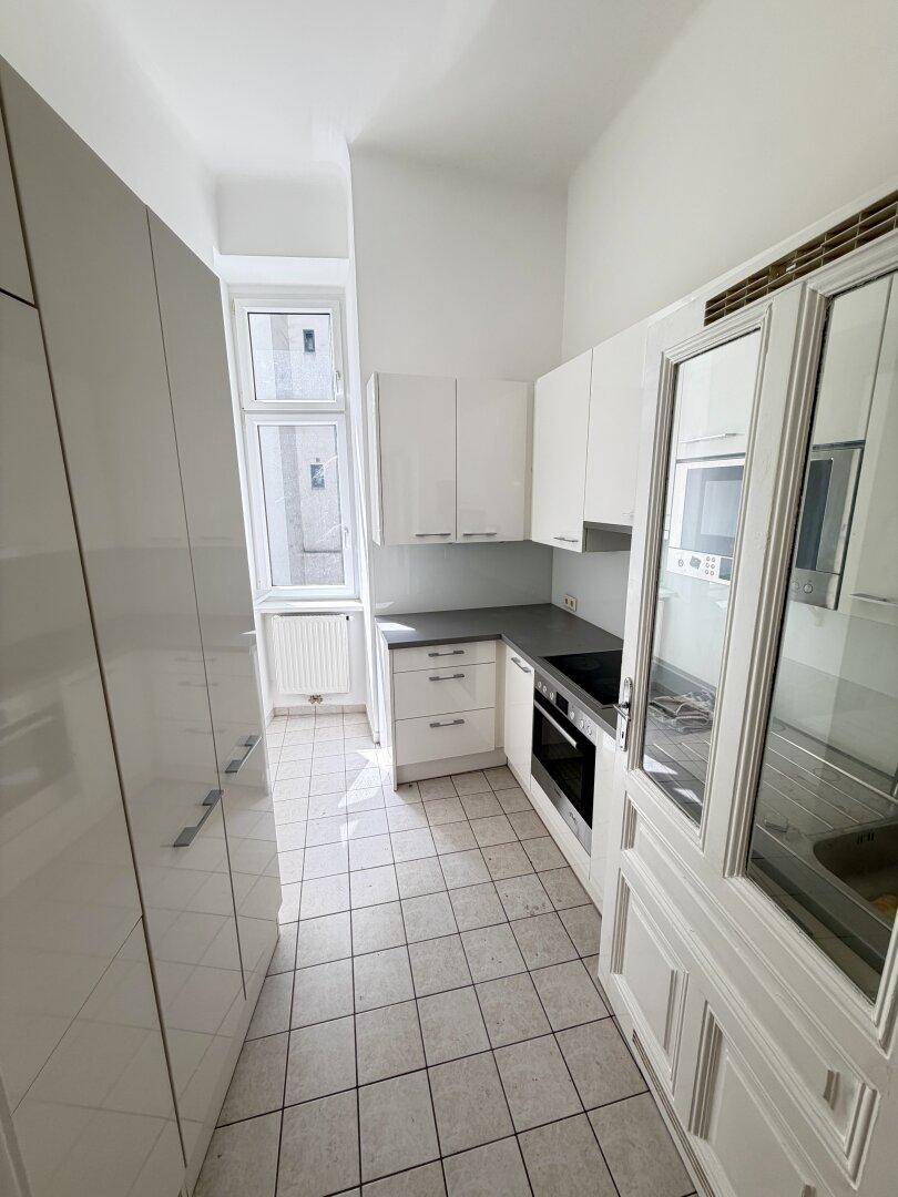 Schmale Küche mit weißen Hochglanzschränken, integriertem Backofen und einem Fenster für Tageslicht.