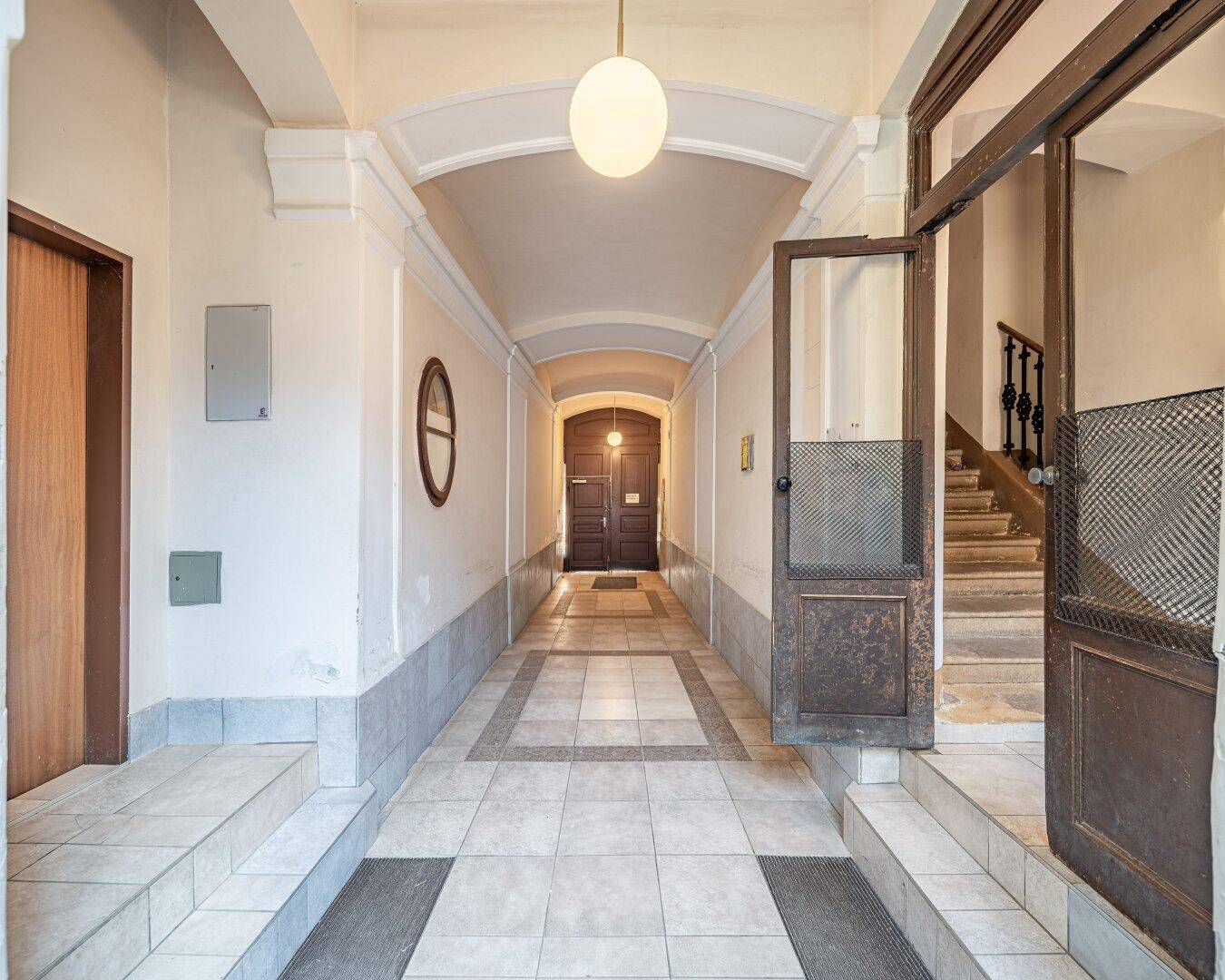 Langer, heller Hausflur mit gemusterten Fliesen und Zugang zum Treppenhaus in einem Altbau.