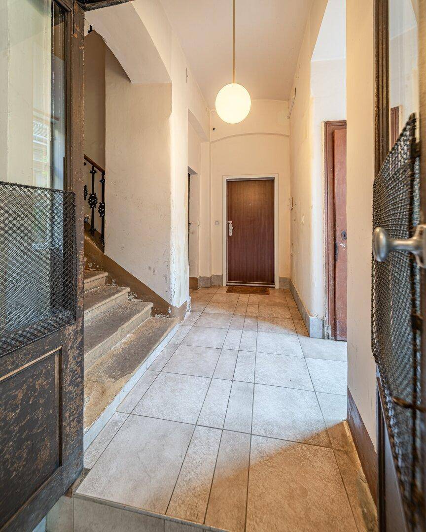 Heller Hausflur mit Fliesenboden, Deckenleuchte und Blick auf das Treppenhaus eines Altbaus.