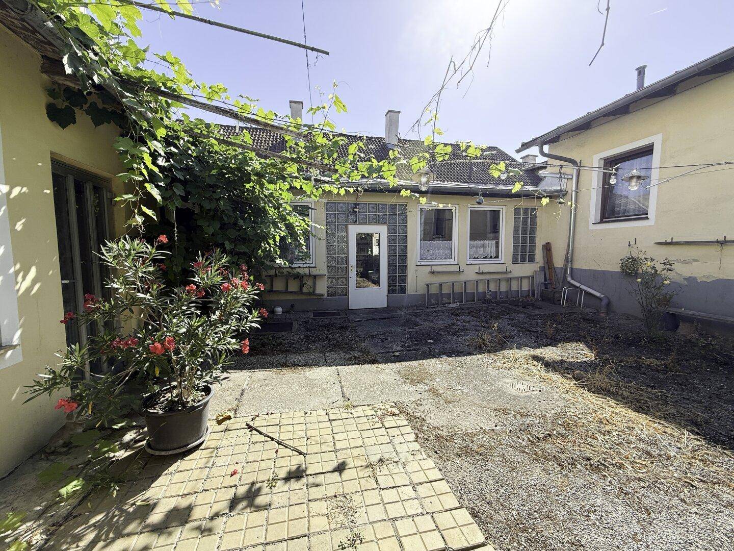 Sonniger Innenhof mit Pflastersteinen, Pflanzen und Zugang zum Gebäude.