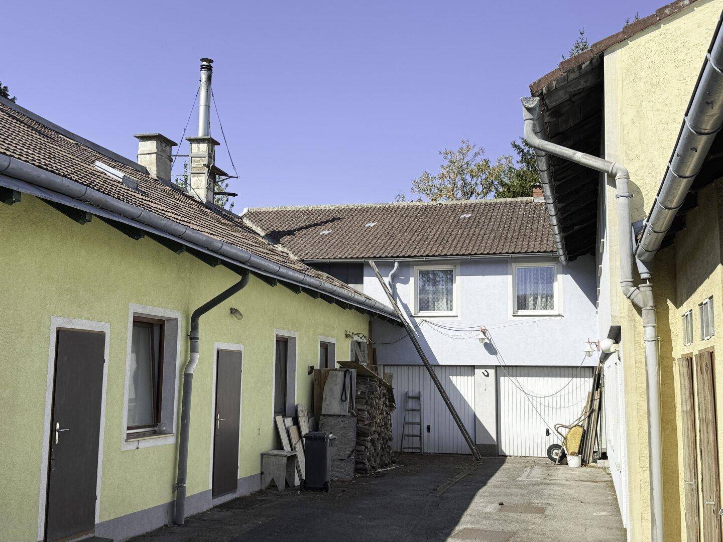 Blick in den Innenhof zwischen den Gebäuden mit Holzstapel und Leiter.