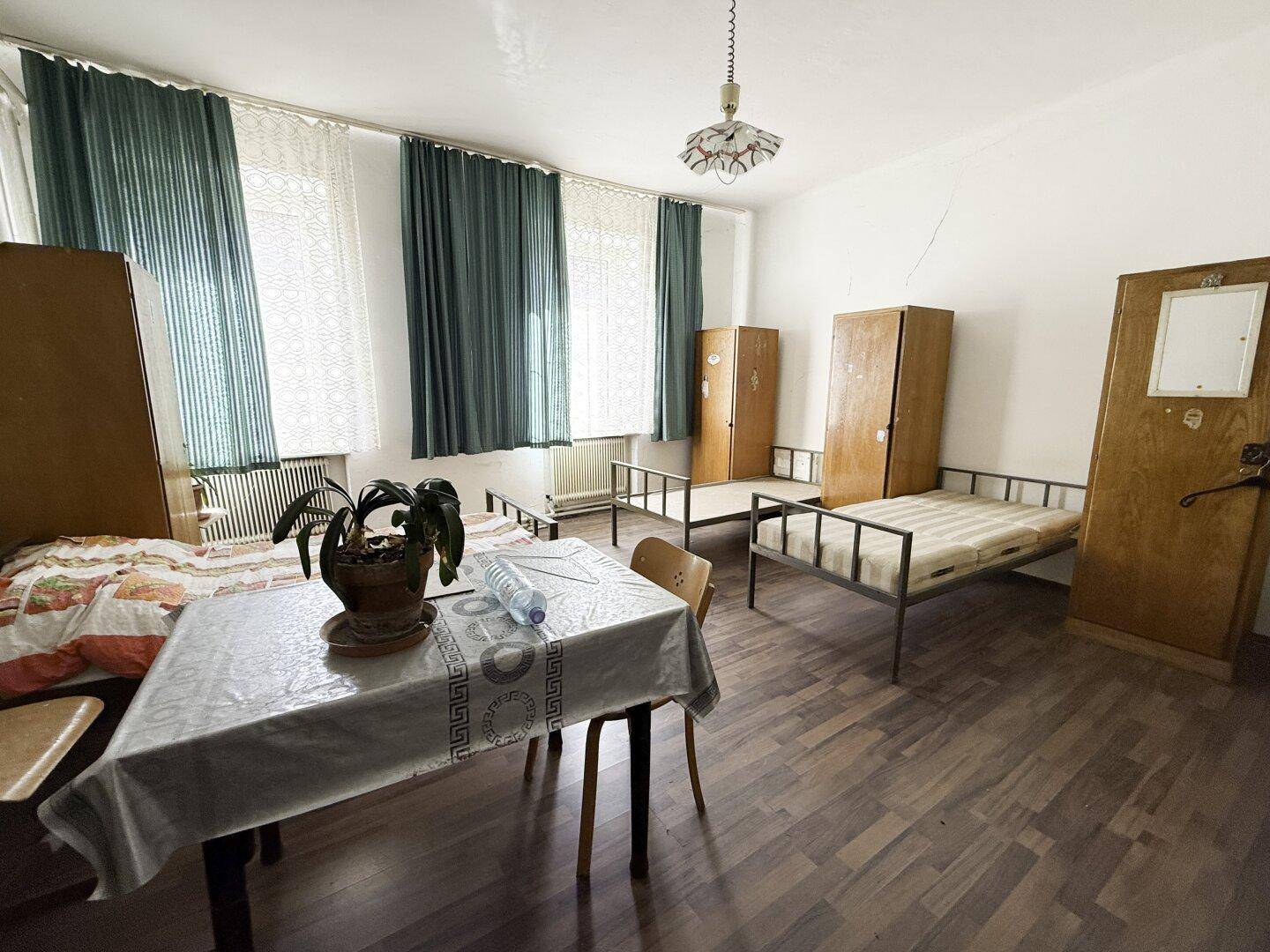 Einfaches Schlafzimmer mit mehreren Betten, Holzschränken und Vorhängen.