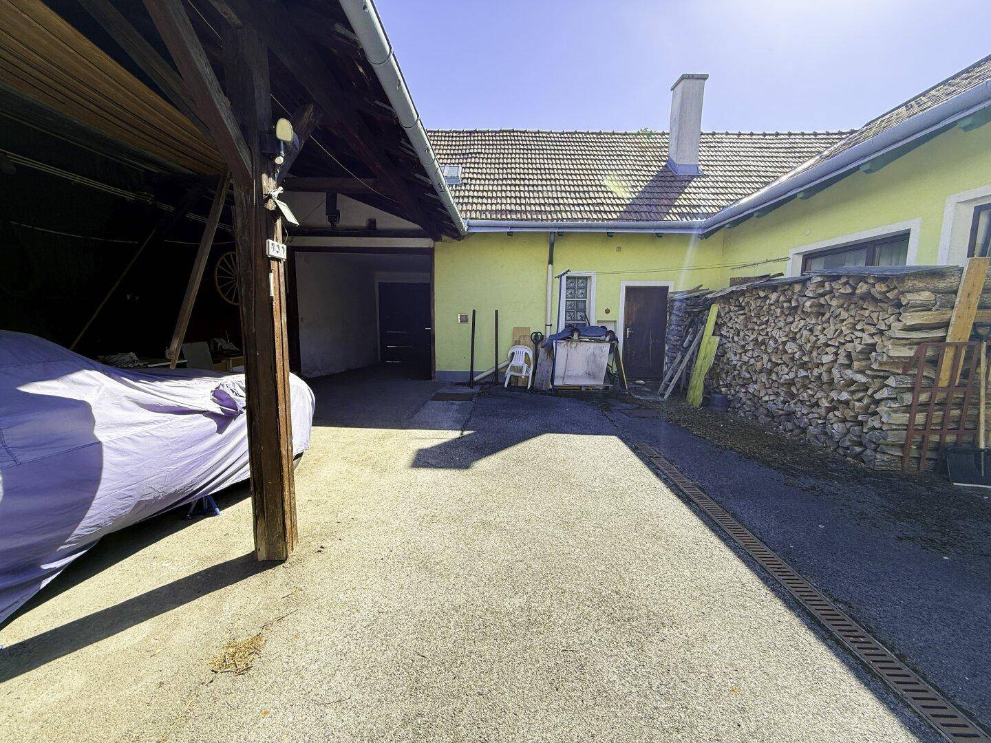 Innenhof mit Carport und Holzstapel, umgeben von Gebäuden.