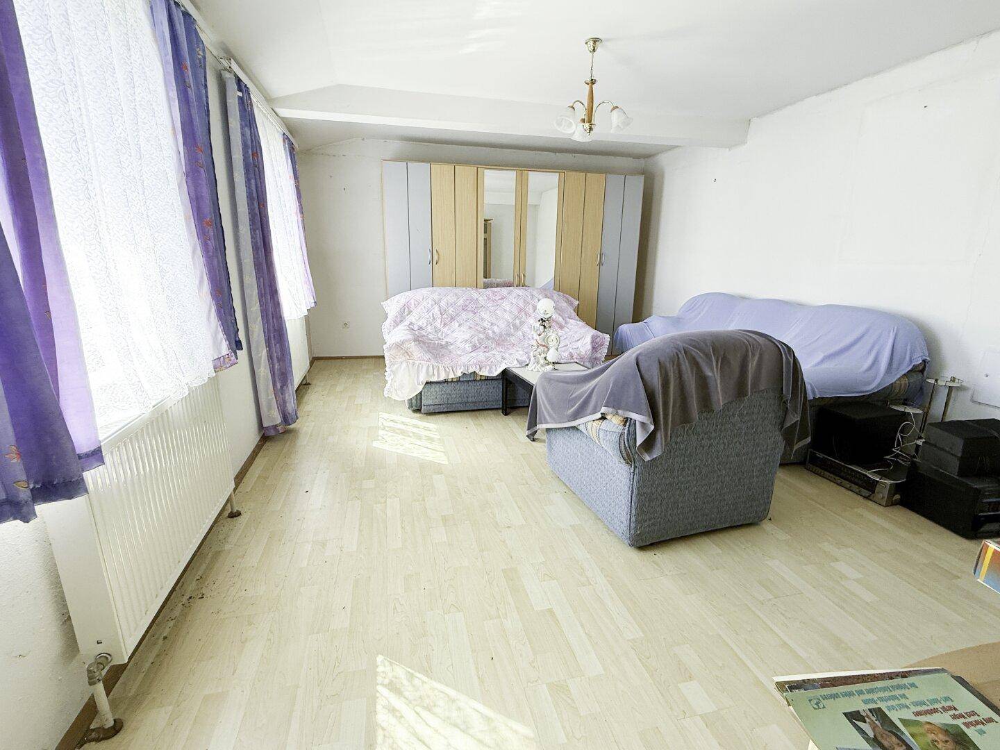 Helles Zimmer mit Laminatboden, großem Schrank und Sitzgelegenheiten.