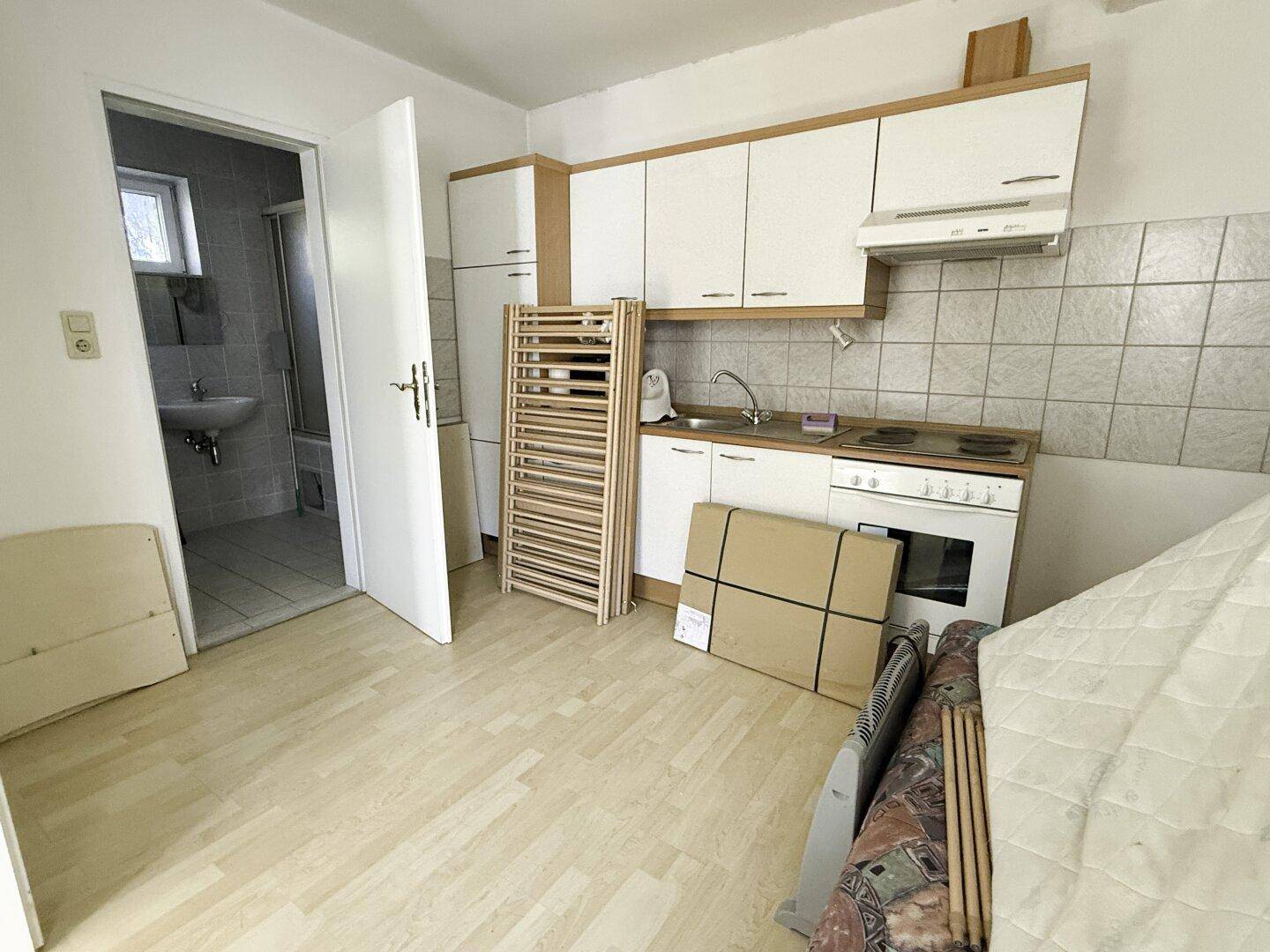 Kleine Küchenzeile mit weißen Schränken, Herd und Zugang zum Badezimmer.