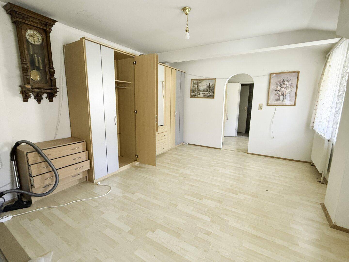 Geräumiges Schlafzimmer mit Laminatboden, großem Kleiderschrank und Wanduhr.