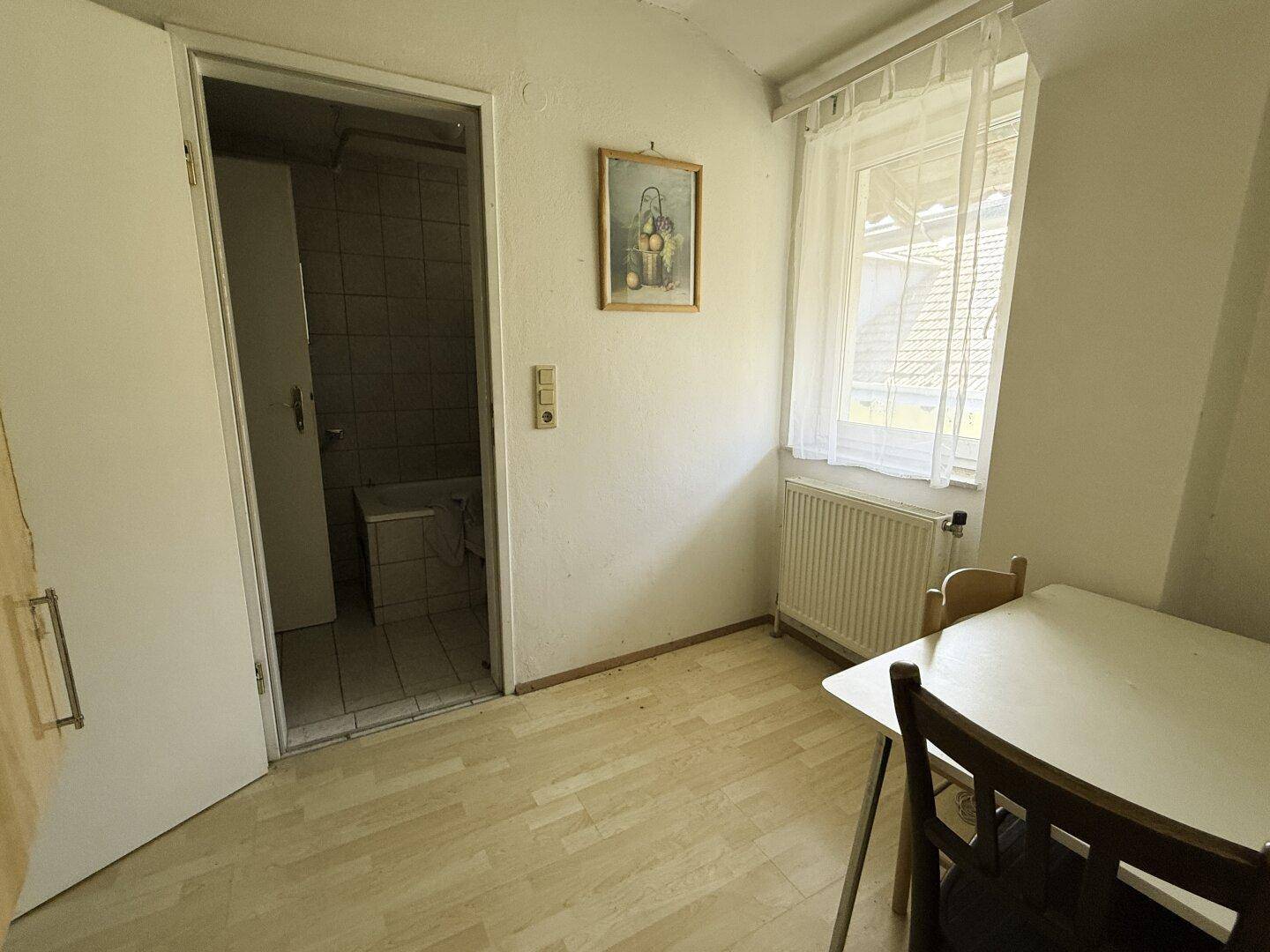 Helles Zimmer mit Tisch, Stühlen und Zugang zu einem Badezimmer.