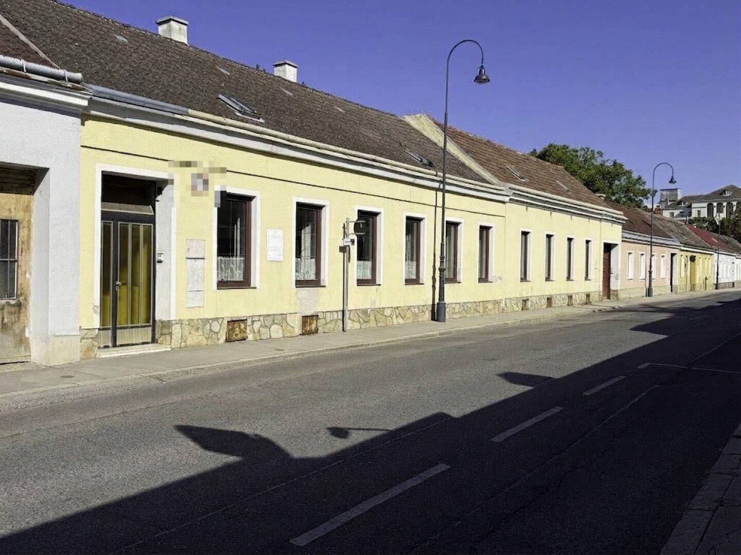 Straßenansicht des historischen Gebäudes mit gelber Fassade und mehreren Fenstern.