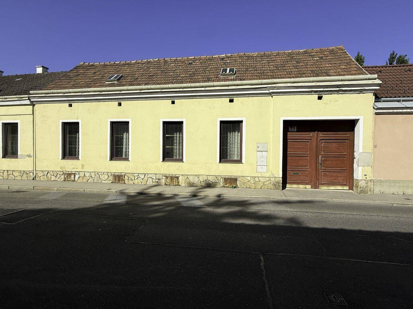 Gelbe Fassade des Gebäudes mit braunem Garagentor und Fenstern zur Straße.