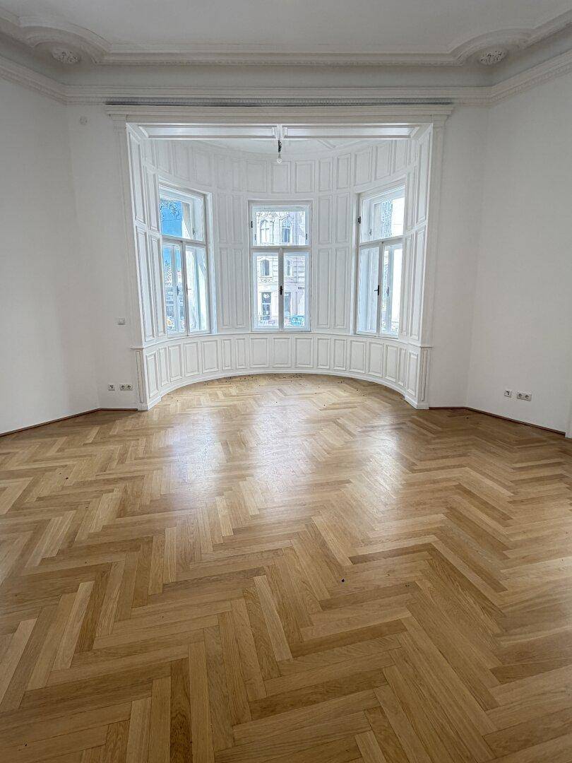 Heller Raum mit elegantem Fischgrätparkett und einem markanten Erkerfenster, das viel Licht spendet.