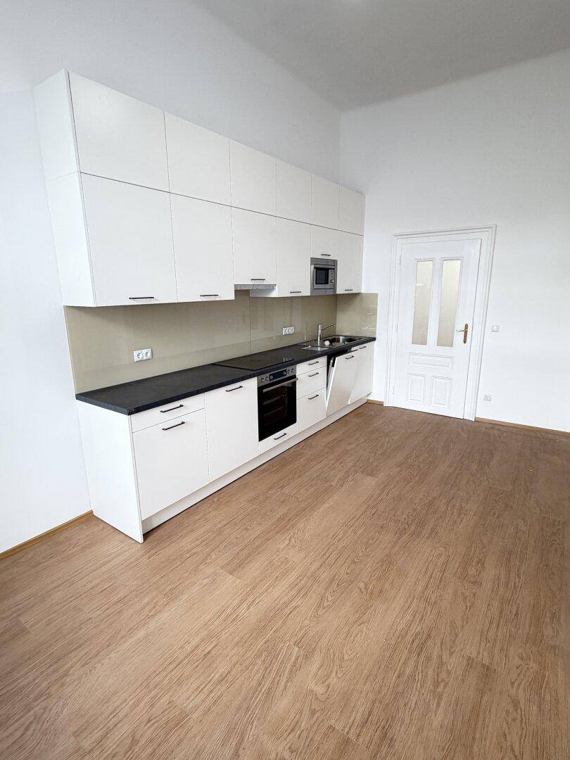 Moderne Einbauküche mit weißen Hochglanzschränken, dunkler Arbeitsplatte und integrierten Geräten.