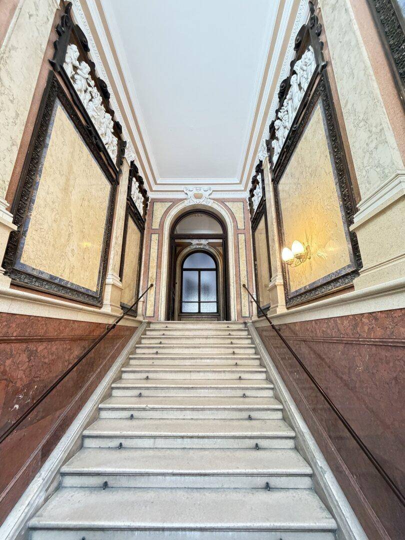 Elegantes Treppenhaus mit Marmorstufen, verzierten Wänden und einem hohen Deckenbereich.