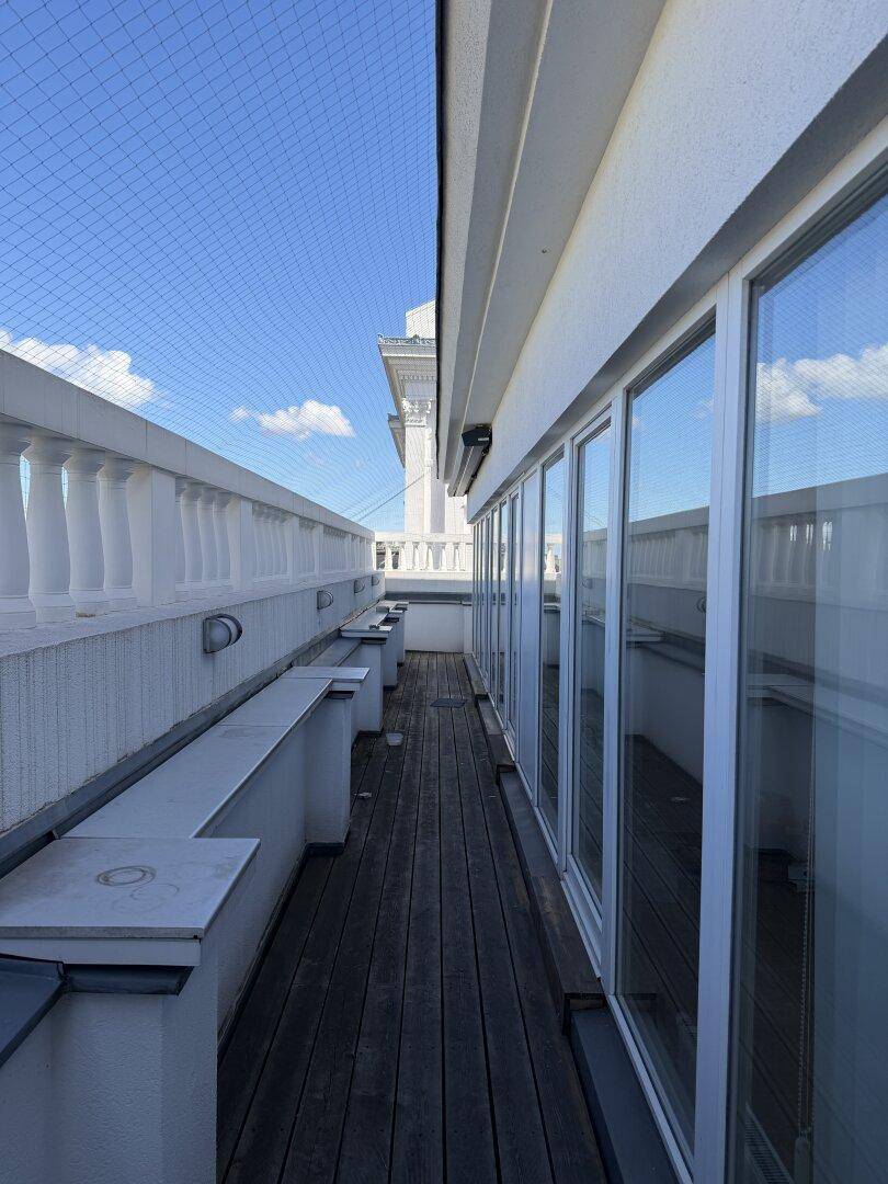 Langer, schmaler Terrassenbereich mit Holzdielen und Balustrade unter blauem Himmel.