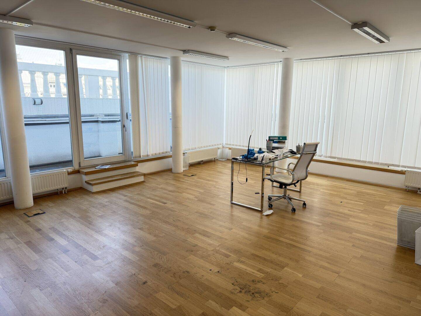 Heller Büroraum mit Holzboden, großzügigen Fenstern und einem Arbeitsplatz.