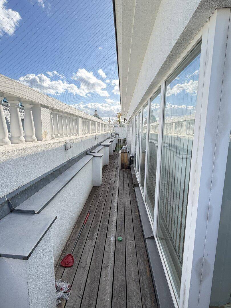 Dachterrasse mit Holzboden, weißer Balustrade und weitem Blick unter blauem Himmel.