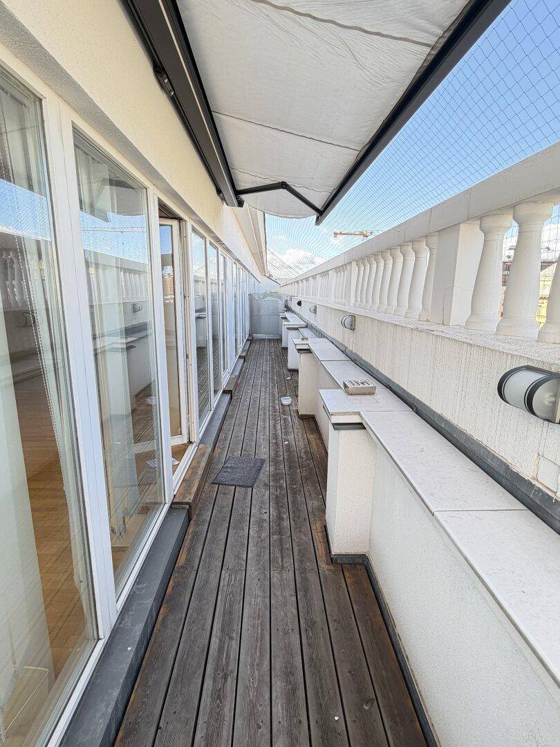 Lange Dachterrasse mit Holzdielen, Markise und Blick auf die Umgebung.