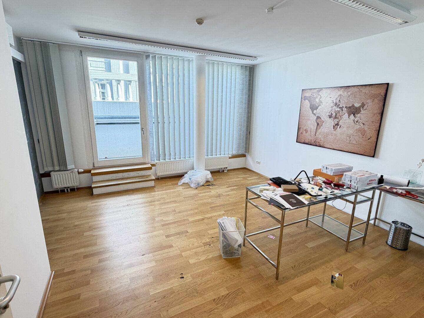 Heller Büroraum mit Holzboden, großen Fenstern und einer Weltkarte an der Wand.
