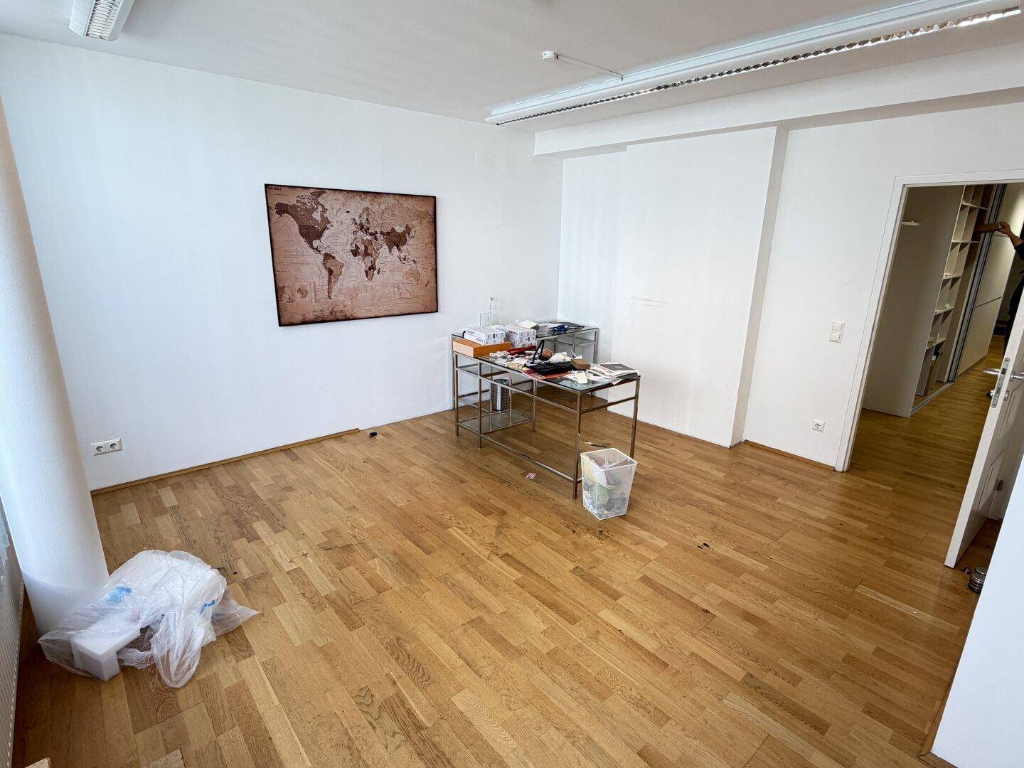 Geräumiges Büro mit Holzboden, weiß gestrichenen Wänden und einem dekorativen Wandbild.