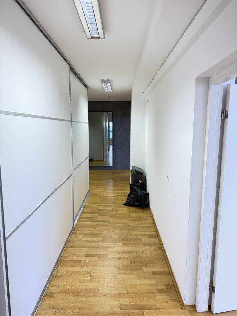 Langer Flur mit Holzboden und weißen Einbauschränken, der zu weiteren Räumen führt.