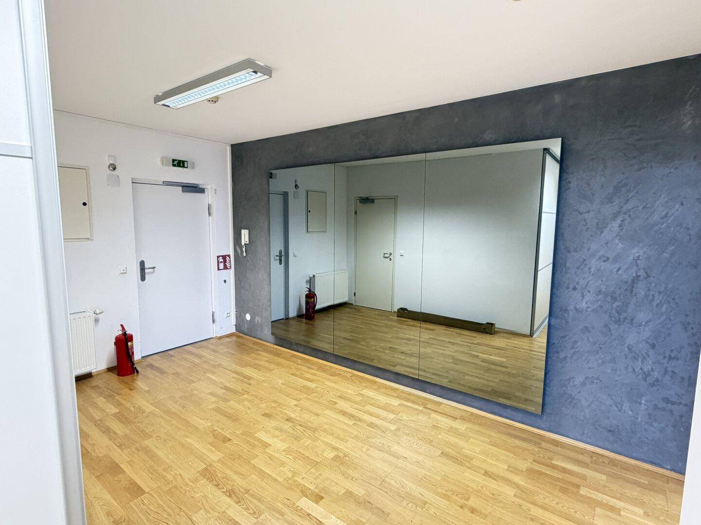 Vielseitiger Raum mit Holzboden, dunkler Akzentwand und großer Spiegelwand.