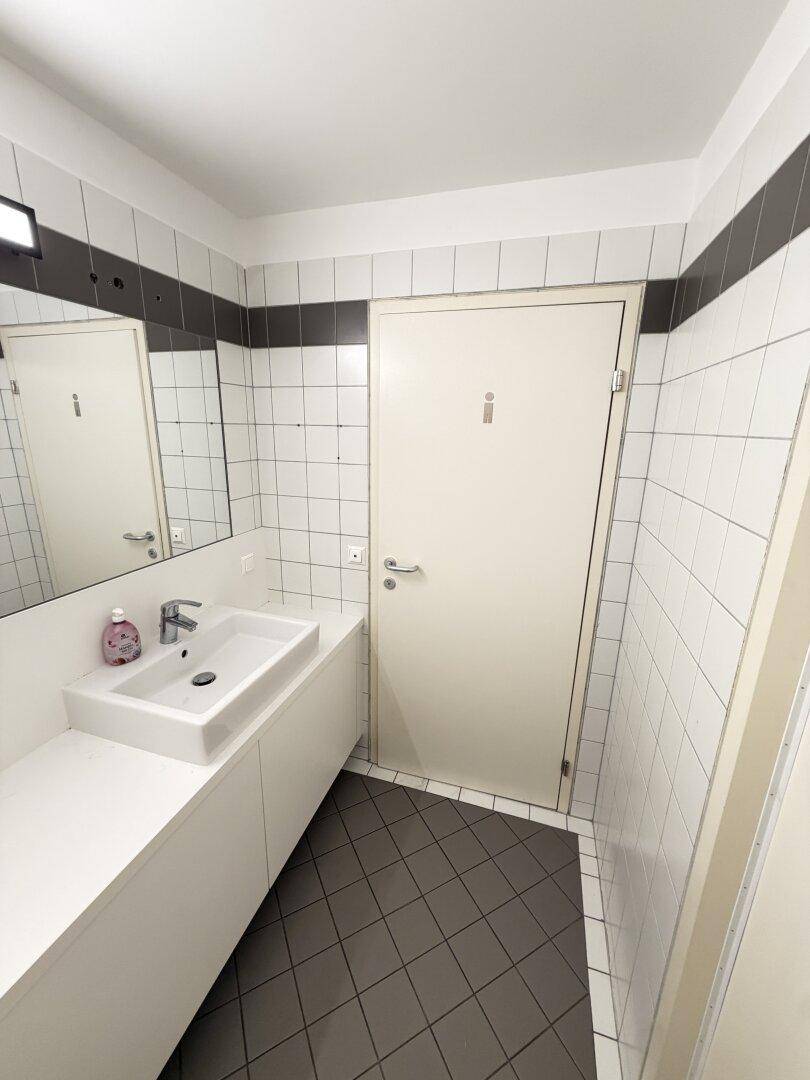Waschraum mit modernem Waschbecken, weißen Wandfliesen und dunklem Boden.