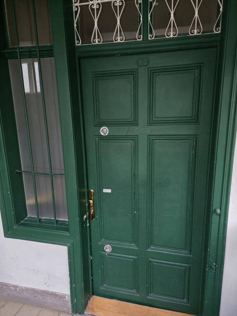 Dunkelgrüne Eingangstür mit dekorativem Gitterwerk und Seitenfenster.