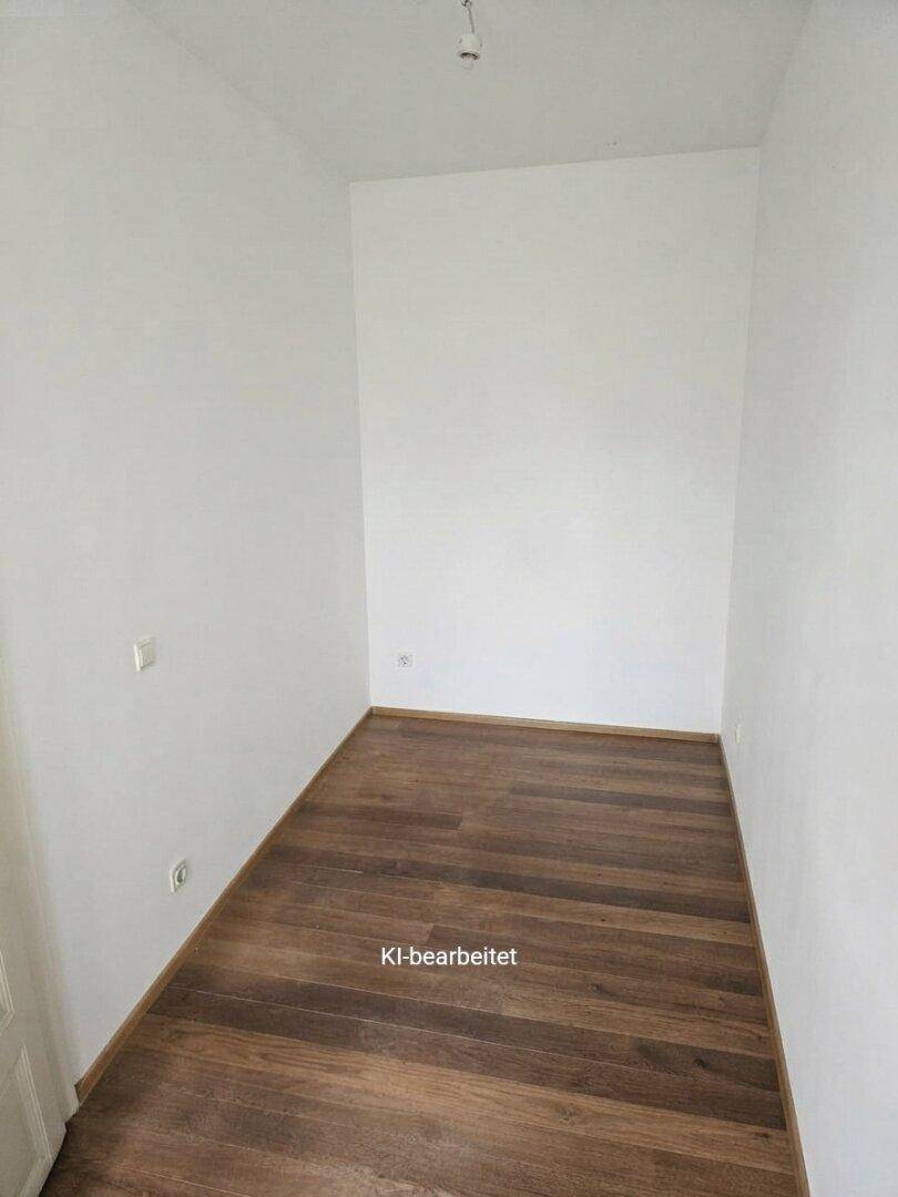 Kleiner, leerer Raum mit dunklem Holzboden und weißen Wänden.