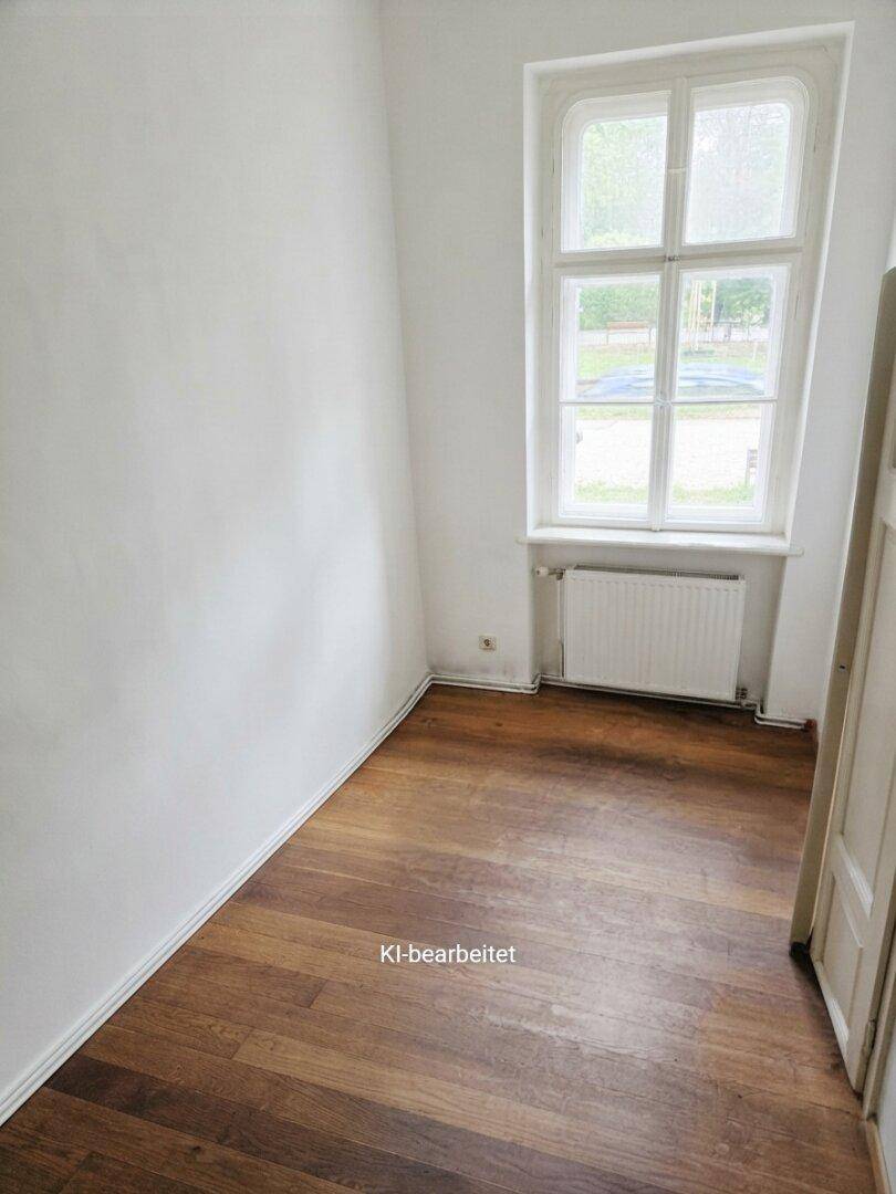 Kleiner Raum mit dunklem Holzboden, weiß gestrichenen Wänden und einem Fenster.