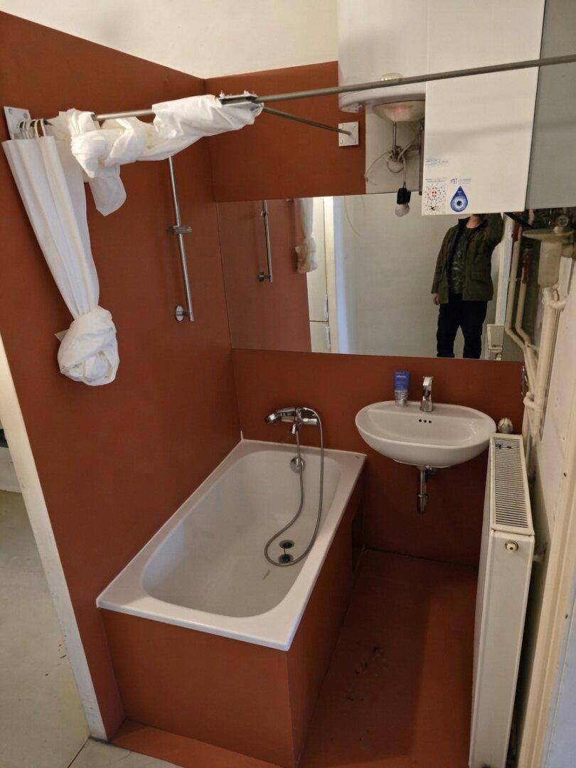 Älteres Badezimmer mit Badewanne, kleinem Waschbecken und orangefarbenen Wänden.