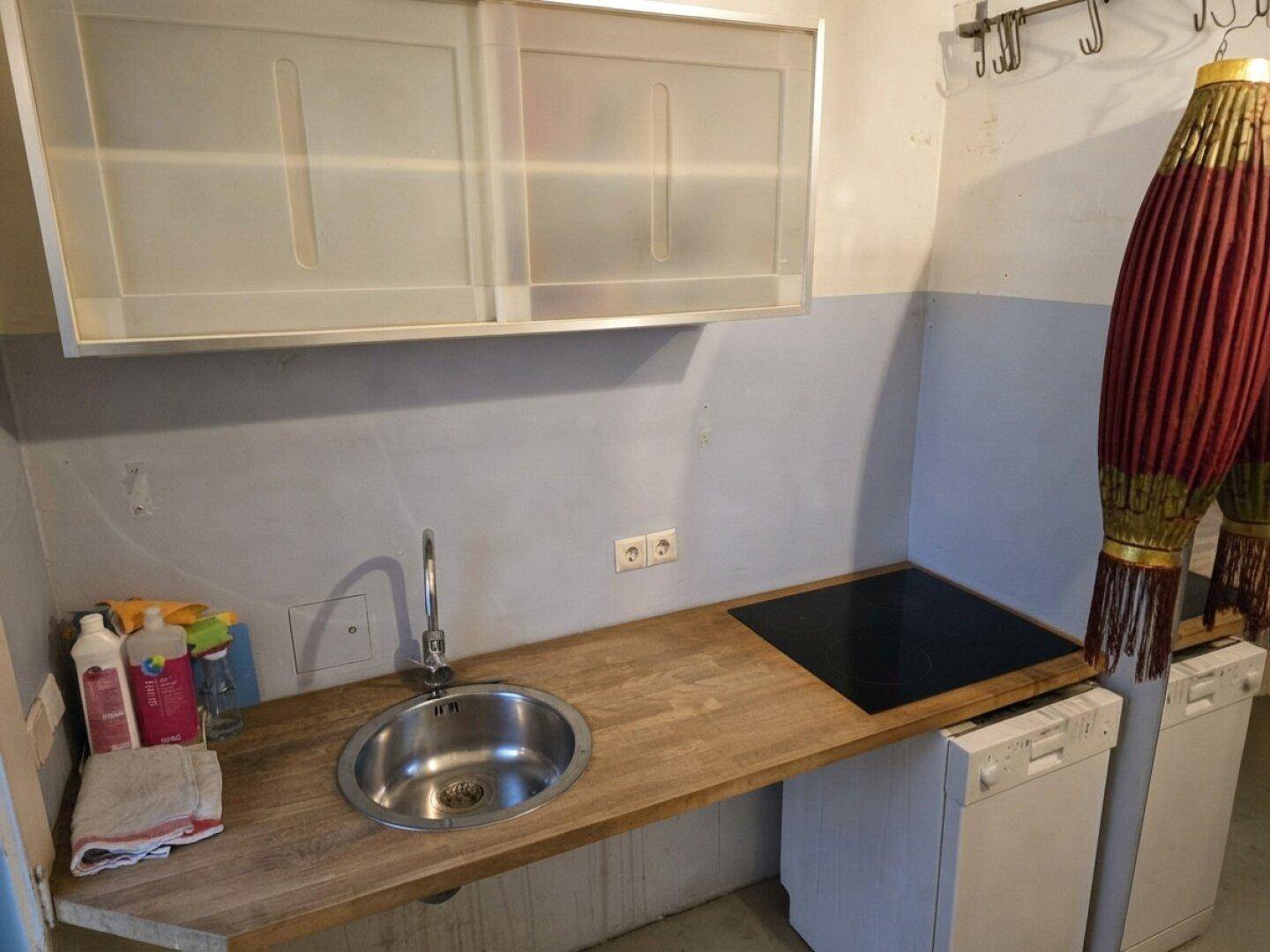 Einfache Küchenzeile mit Spüle, Kochfeld und älteren Hängeschränken.