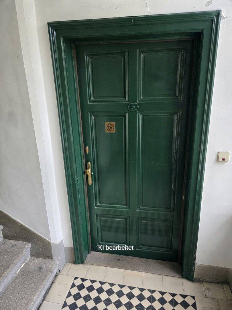 Dunkelgrüne Eingangstür mit traditionellem Kassettenmuster und schwarz-weißem Fliesenboden im Treppenhaus.
