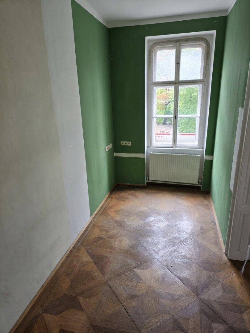 Schmaler Raum mit Parkettboden und grünen Akzentwänden, ideal als Schlaf- oder Arbeitszimmer.