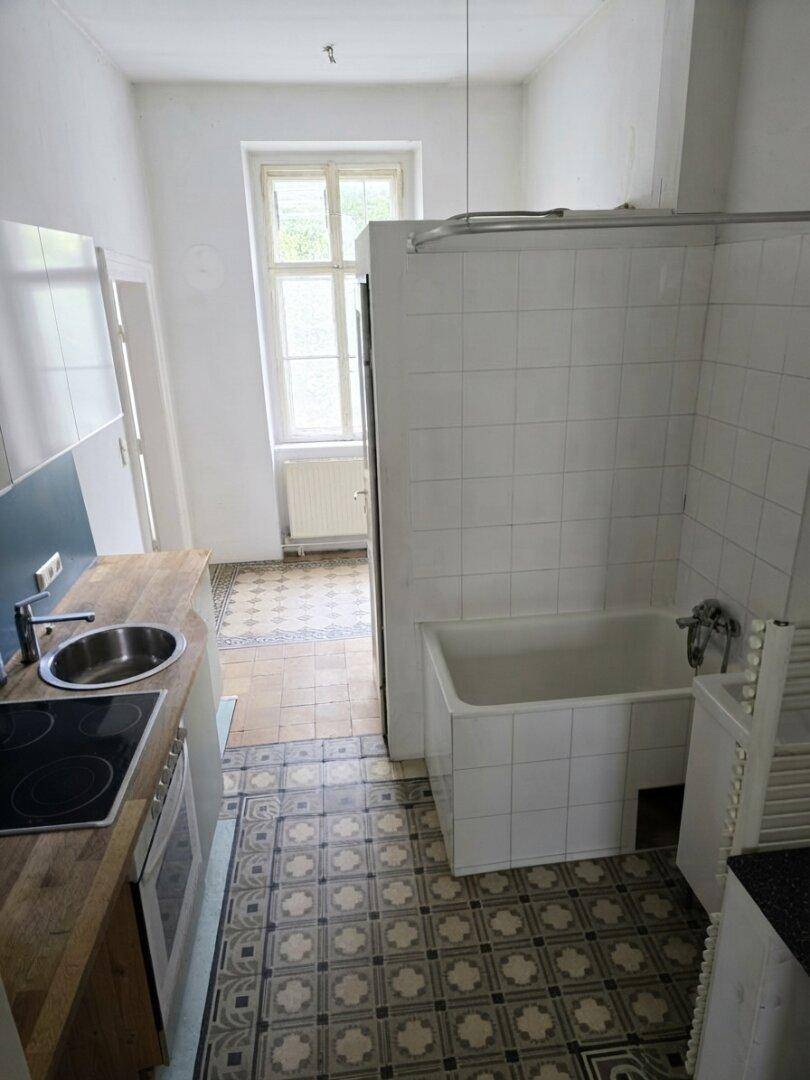 Ungewöhnliche Kombination aus Küchenzeile und Badewanne in einem Raum mit gemustertem Fliesenboden.