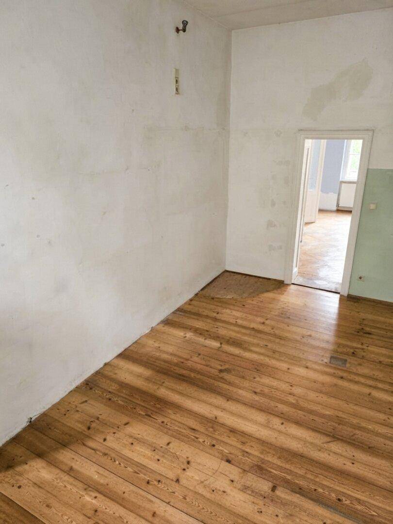 Geräumiger Raum mit Dielenboden und weißen Wänden, der auf eine Renovierung wartet.