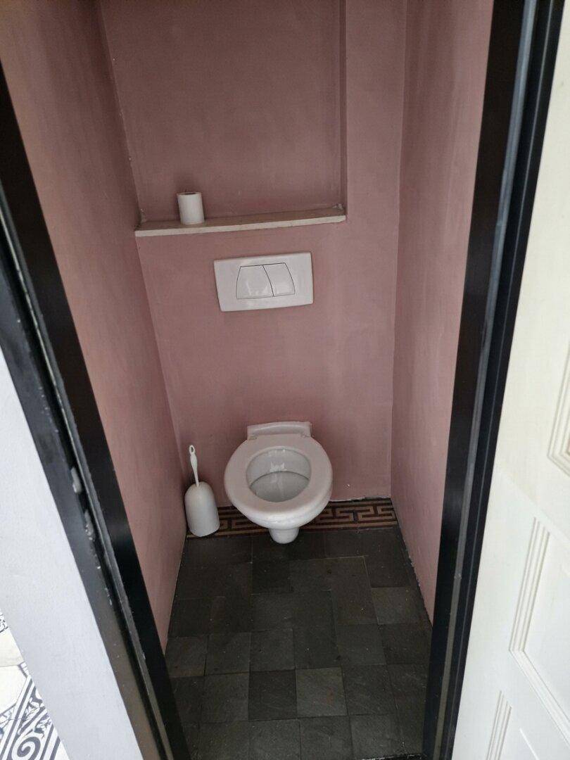 Kleines Gäste-WC mit rosa Wänden, dunklem Fliesenboden und wandhängender Toilette.