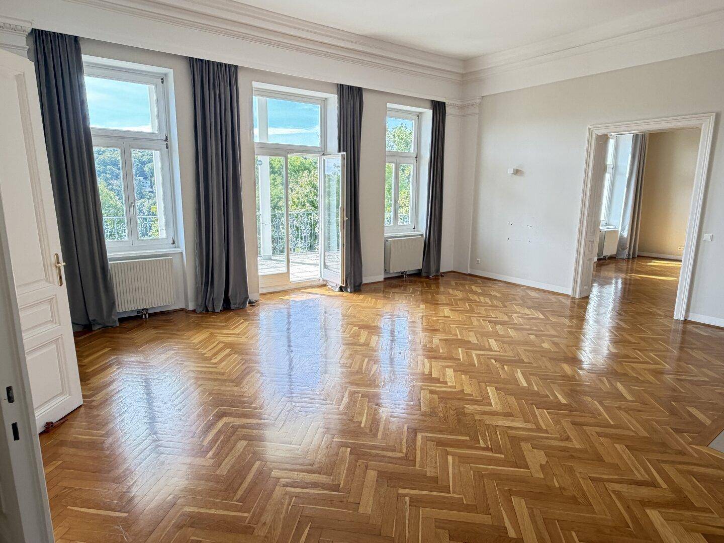 Helles Wohnzimmer mit Fischgrätparkett, hohen Decken und Zugang zu einem französischen Balkon.