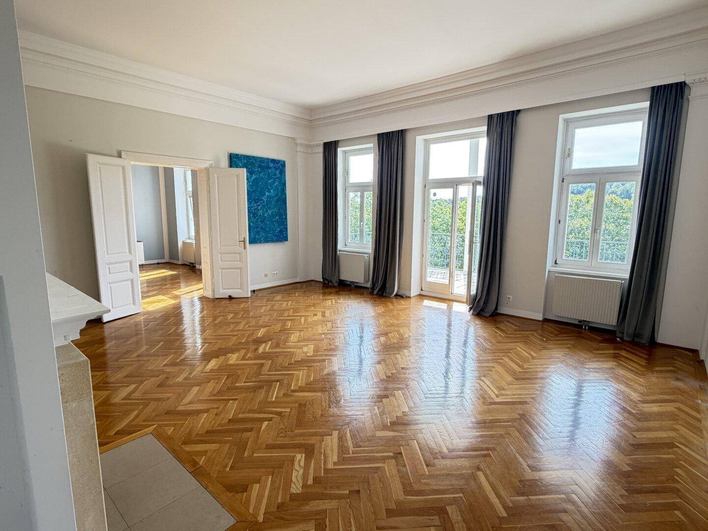 Großzügiges Wohnzimmer mit Fischgrätparkett, hohen Decken und Zugang zum Balkon.