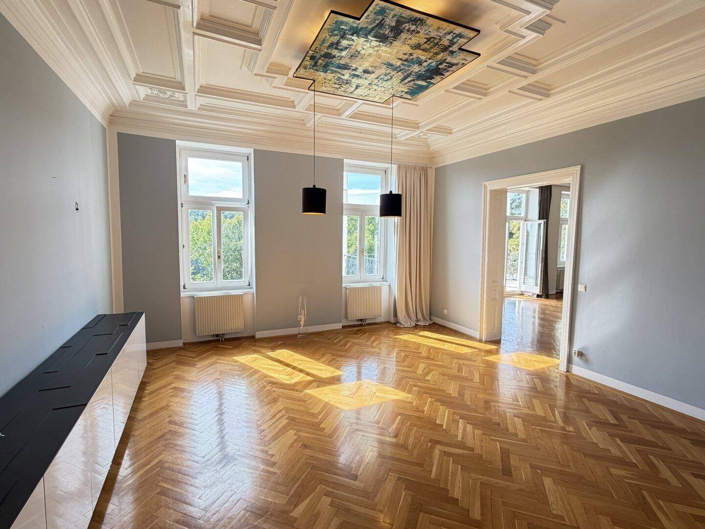 Elegantes Wohnzimmer mit Fischgrätparkett, Kassettendecke und modernen Hängelampen.