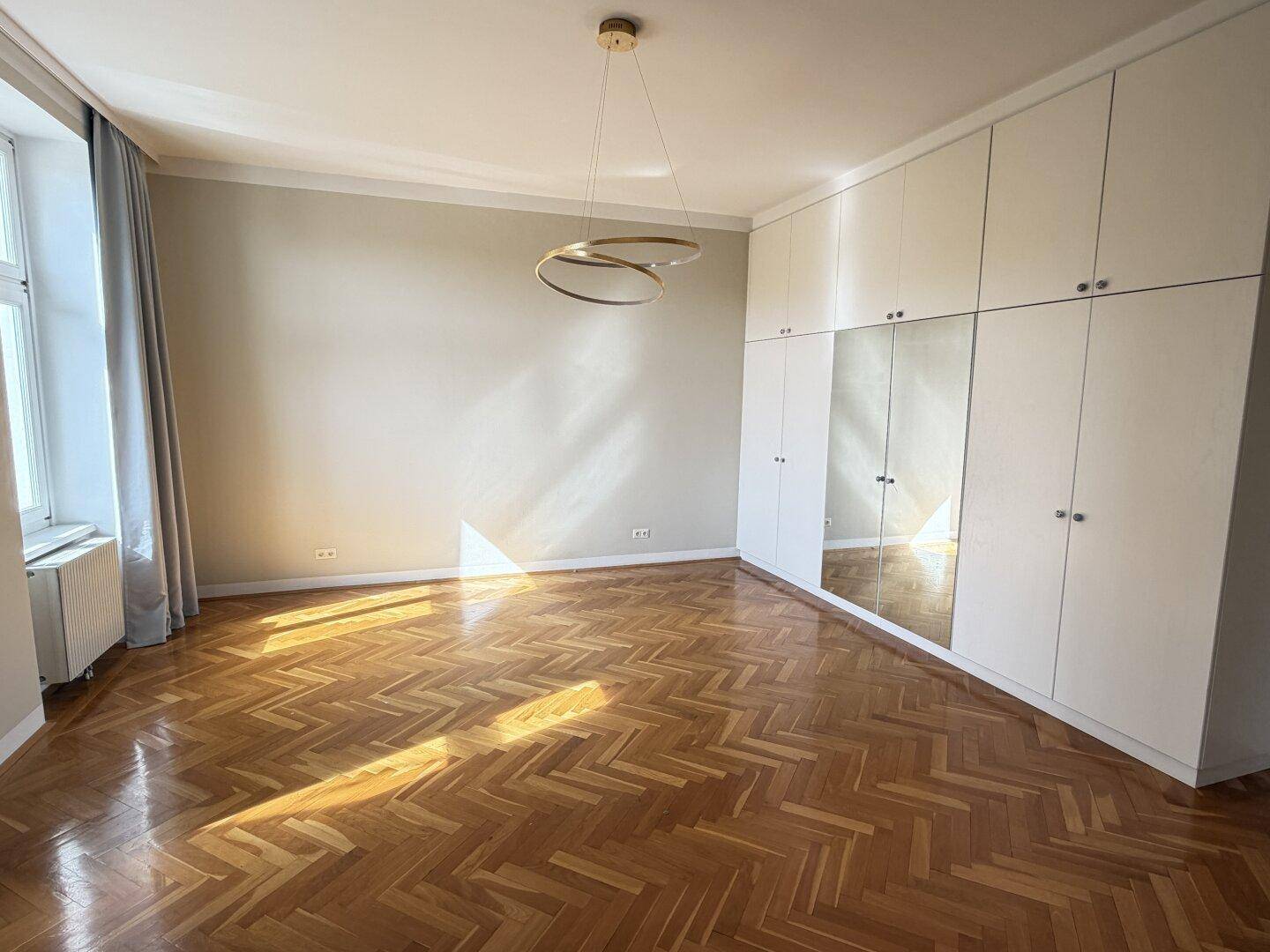 Geräumiges Schlafzimmer mit Fischgrätparkett, Einbauschränken und Spiegelfronten.
