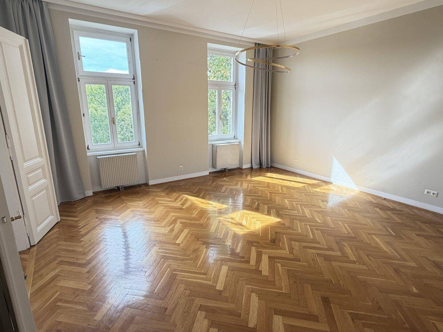 Helles Schlafzimmer mit Fischgrätparkett, hohen Decken und großen Fenstern.