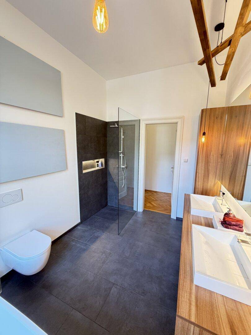 Modernes Badezimmer mit Doppelwaschbecken, ebenerdiger Dusche und dunklen Fliesen.