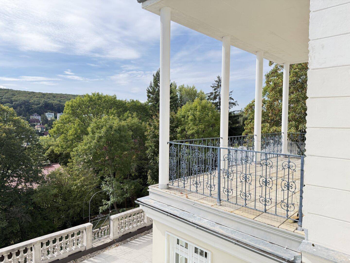 Weitläufige Terrasse mit Säulen und schmiedeeisernem Geländer, umgeben von viel Grün.